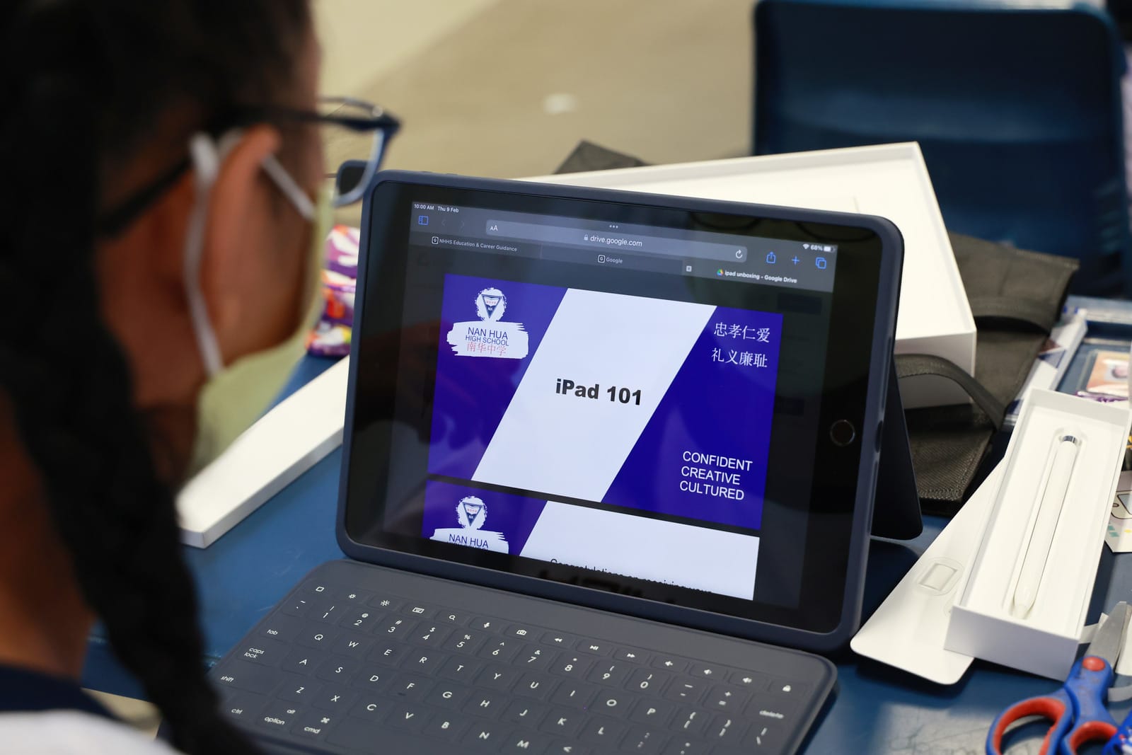 A masked student looks at an iPad displaying an "iPad 101" presentation from Nan Hua High School, with a keyboard attached.